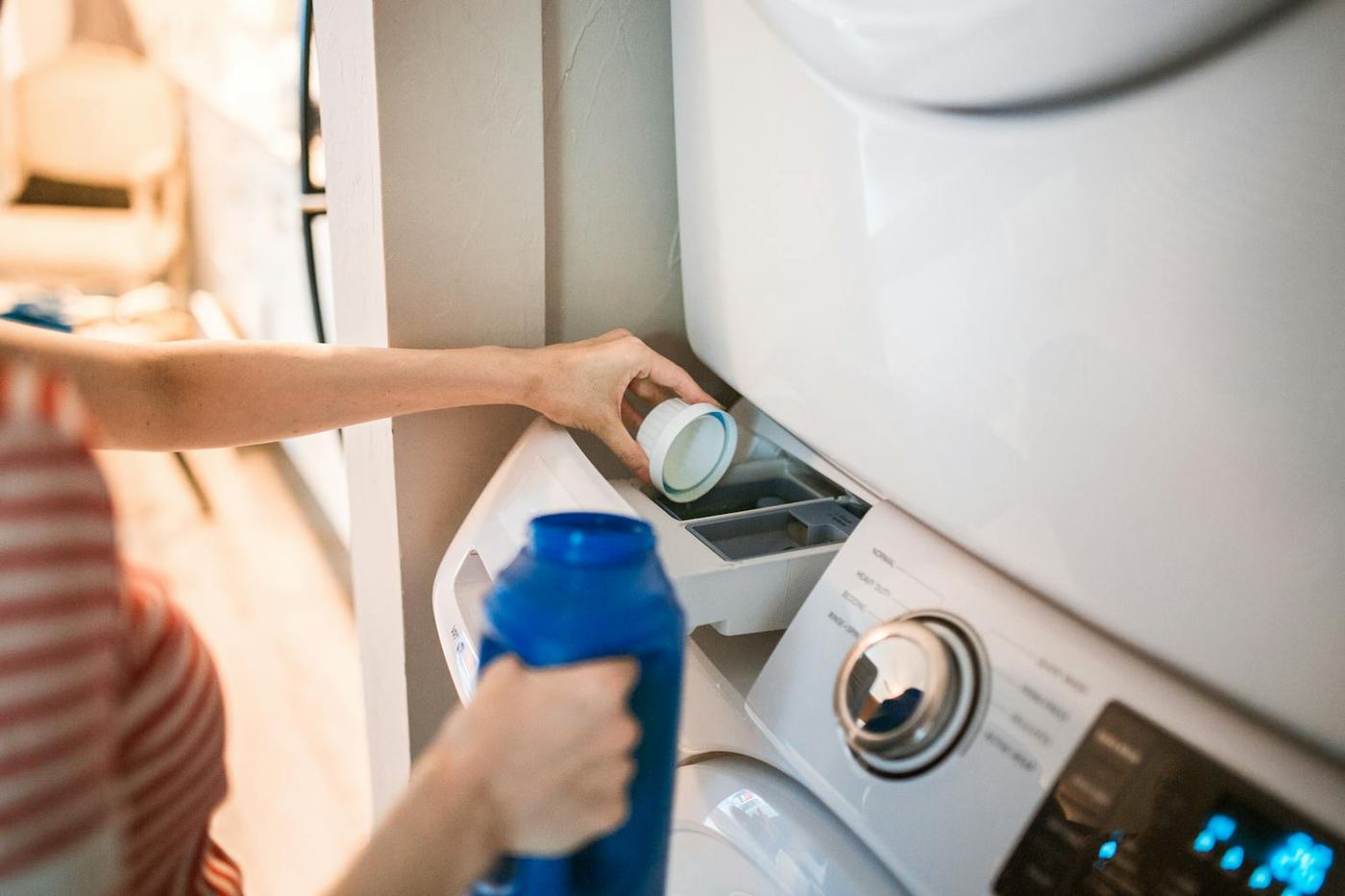 Close up of a person pouring detergent into a front loading washer emphasizing household chores