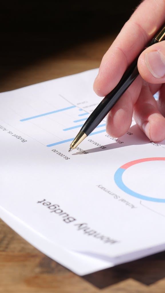 Close up of hand analyzing data on a monthly budget document with graphs and charts