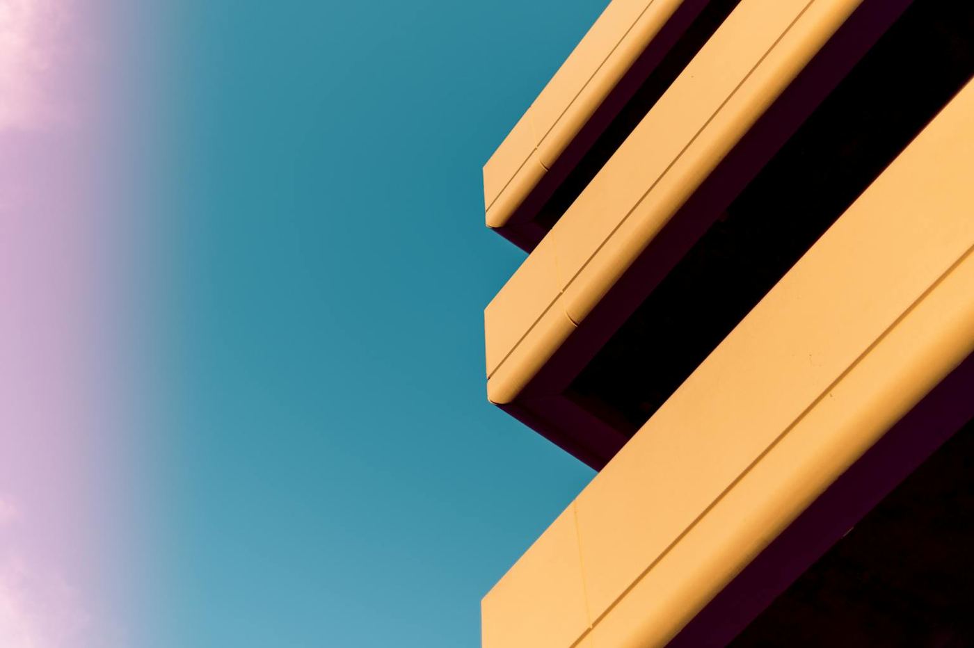 From below of exterior fragment of modern building with big terraces against cloudless blue sky on sunny day