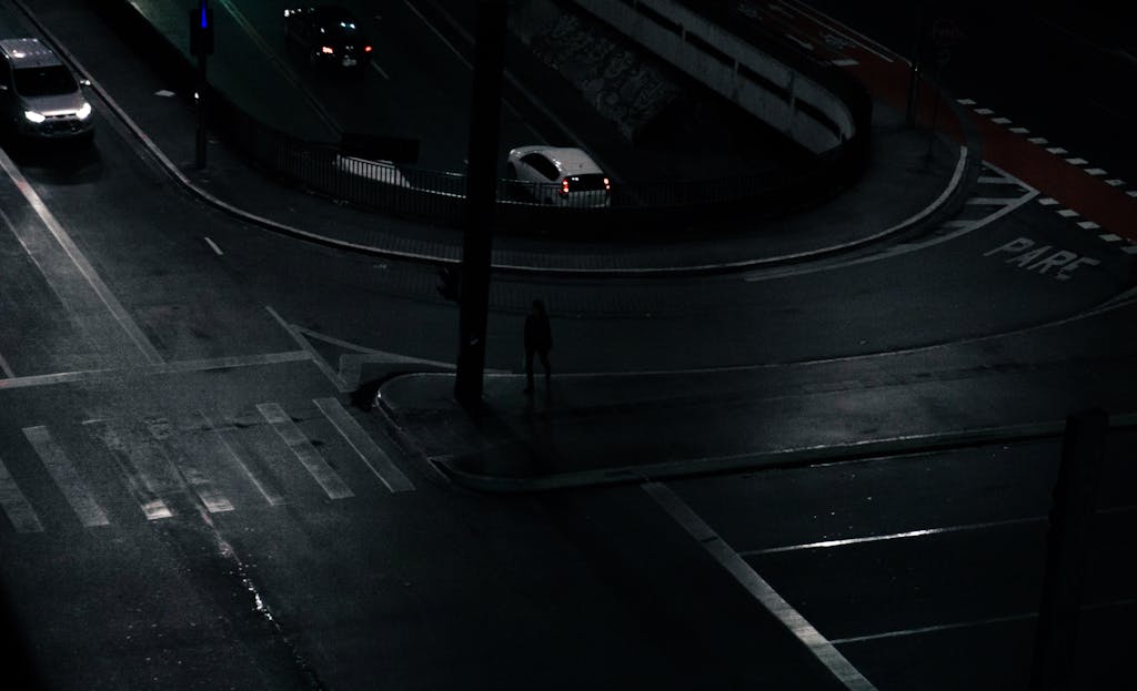 Nighttime urban intersection with cars and dim street lighting.