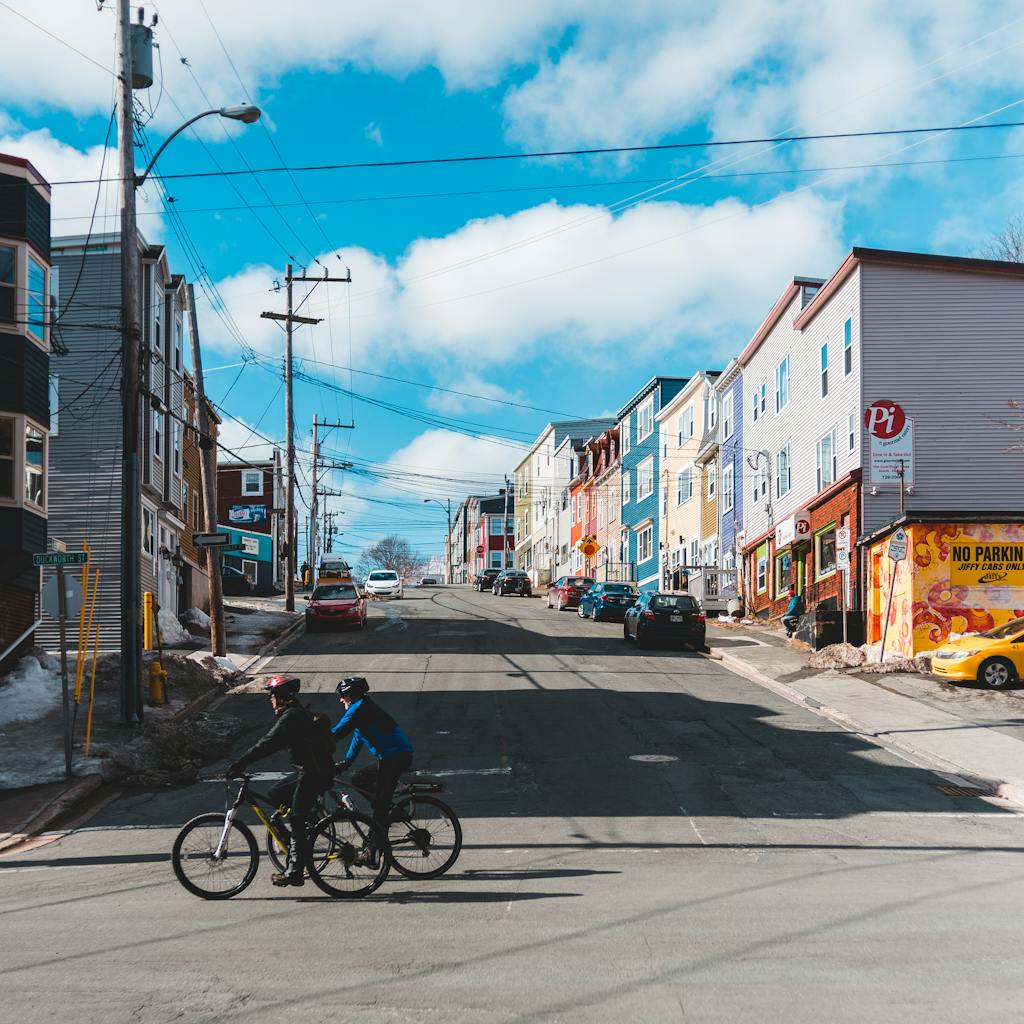 Two cyclists ride through a vibrant urban area lined with colorful buildings on a sunny day.